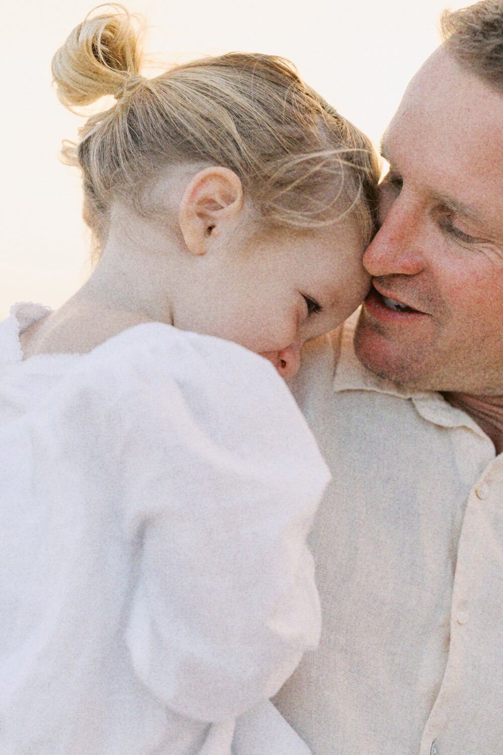 A father tenderly nuzzles his young blonde daughter in a heartwarming beach portrait.