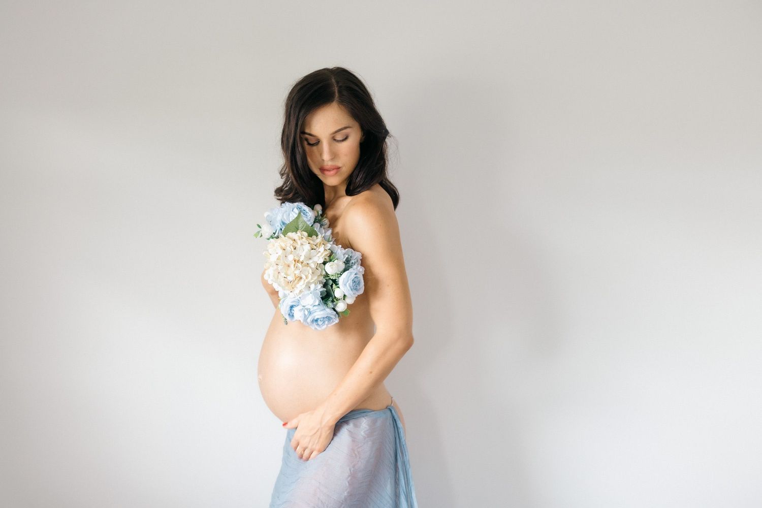 An elegant maternity photo featuring soft blue fabric and delicate white flowers against a minimal backdrop.