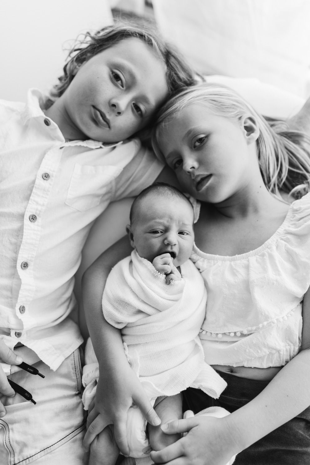 A baby and parent lie together in white clothing on a light background.