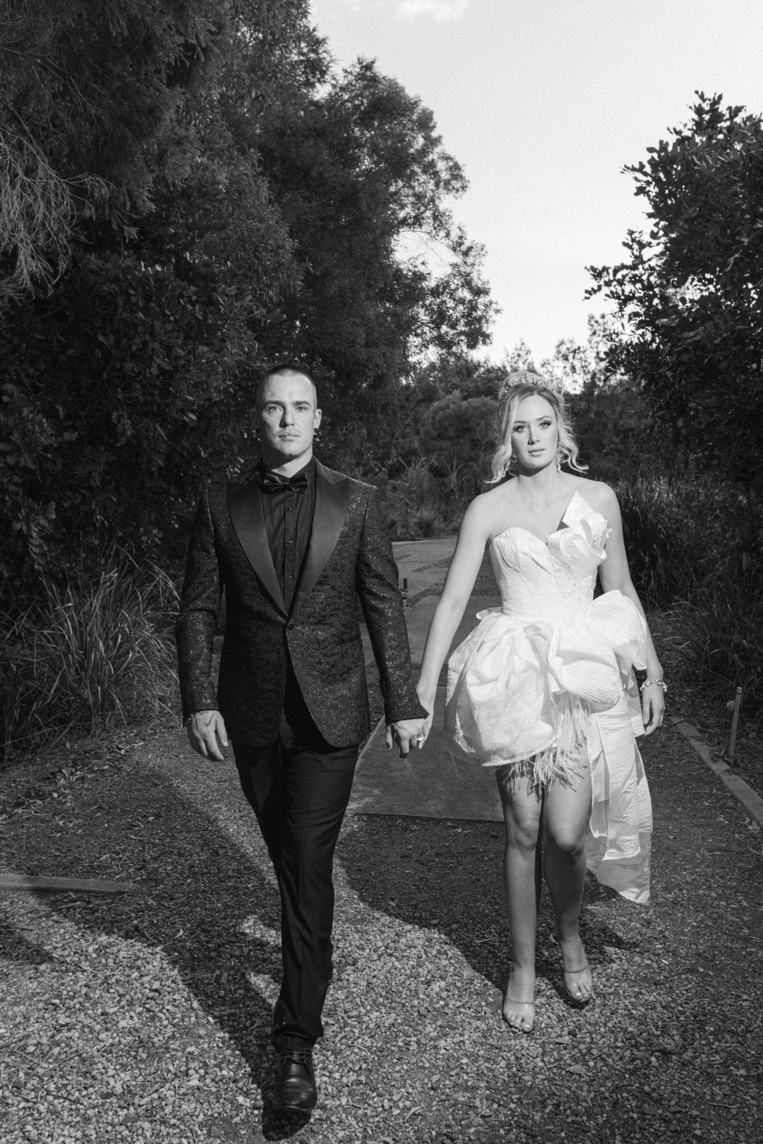 Black and white wedding photography series on a gravel path surrounded by trees.