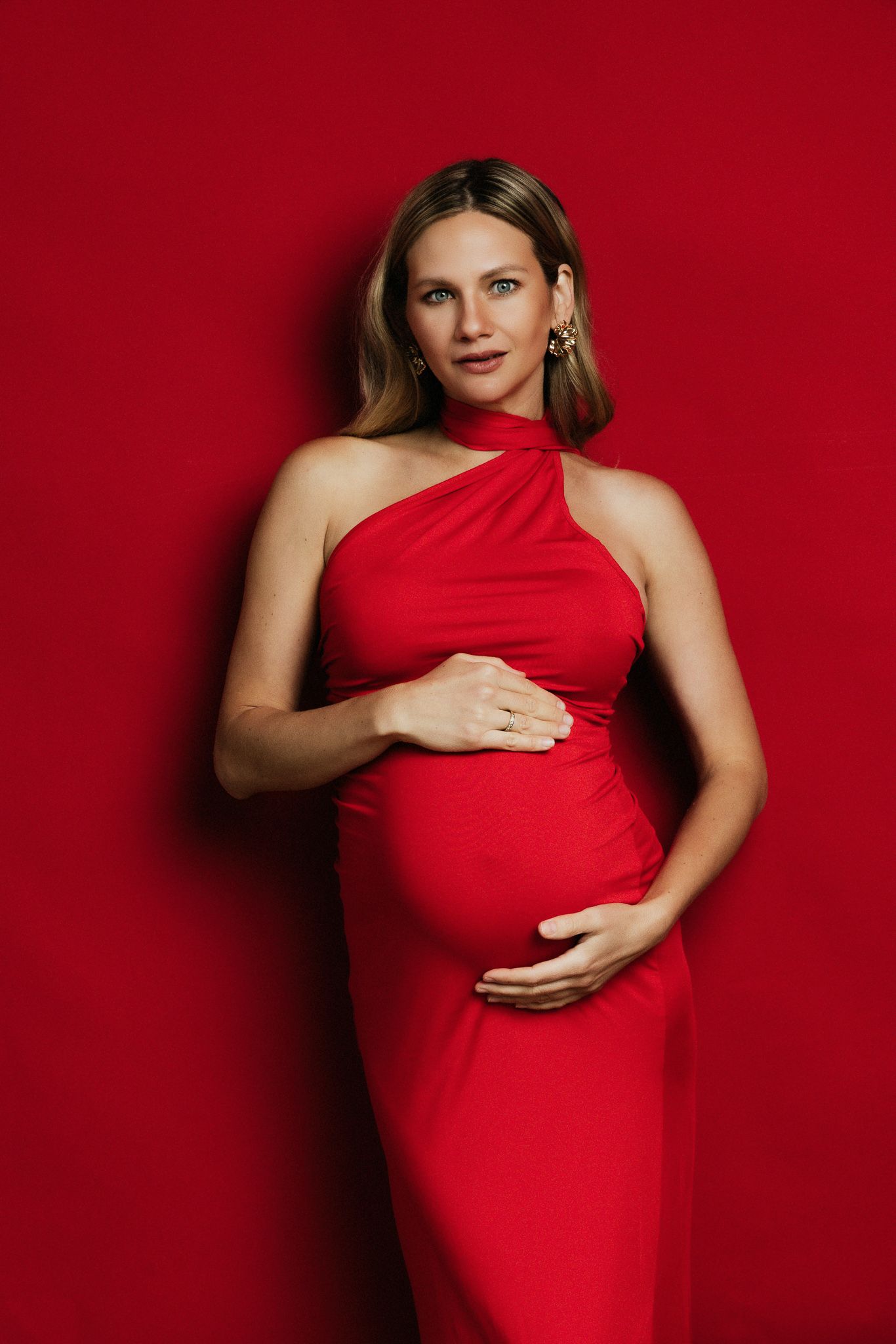 Maternity photo series showing a pregnant woman in a red dress against a red background posing in different angles.