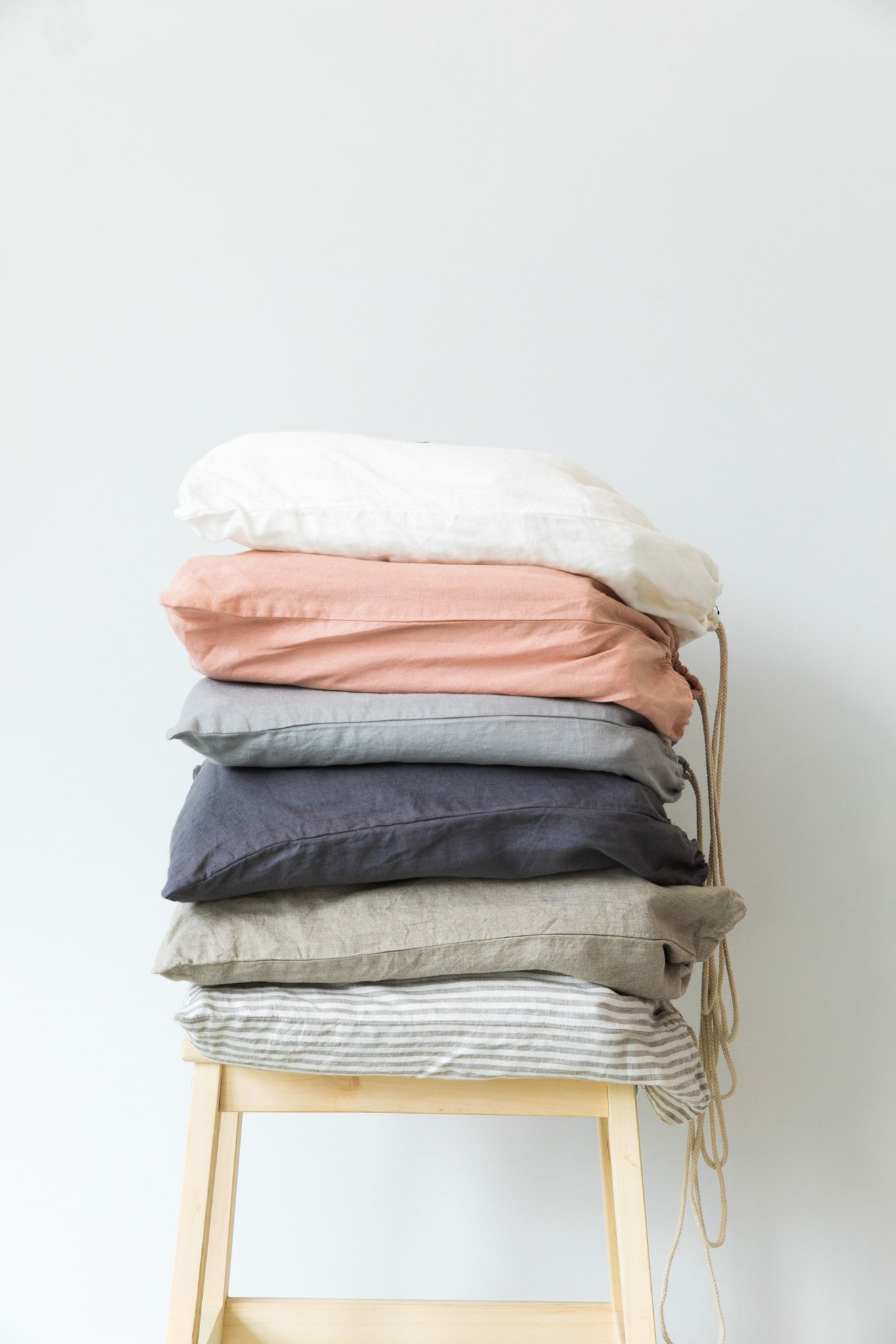 Stack of folded bedding and linens in neutral colors displayed on wooden stool.