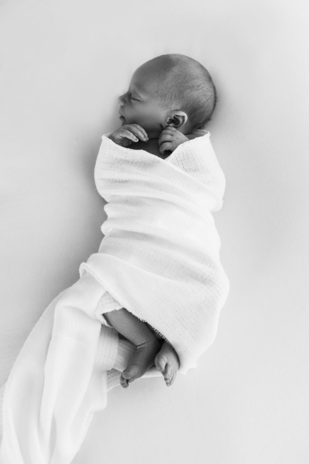 Newborn baby wrapped in white blanket photographed in black and white.