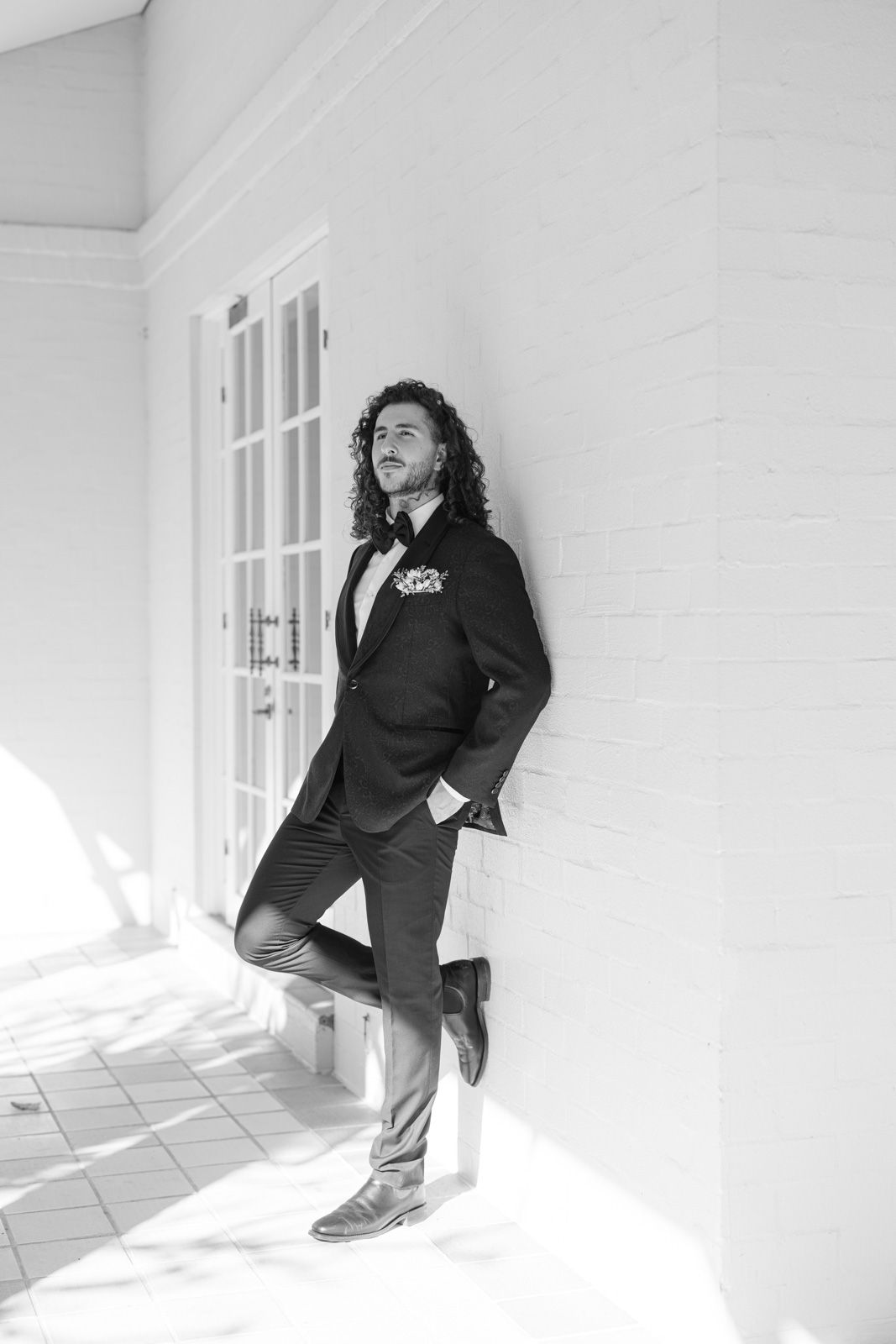 Black and white photo series showing someone in casual attire sitting and posing against a bright white wall with windows.
