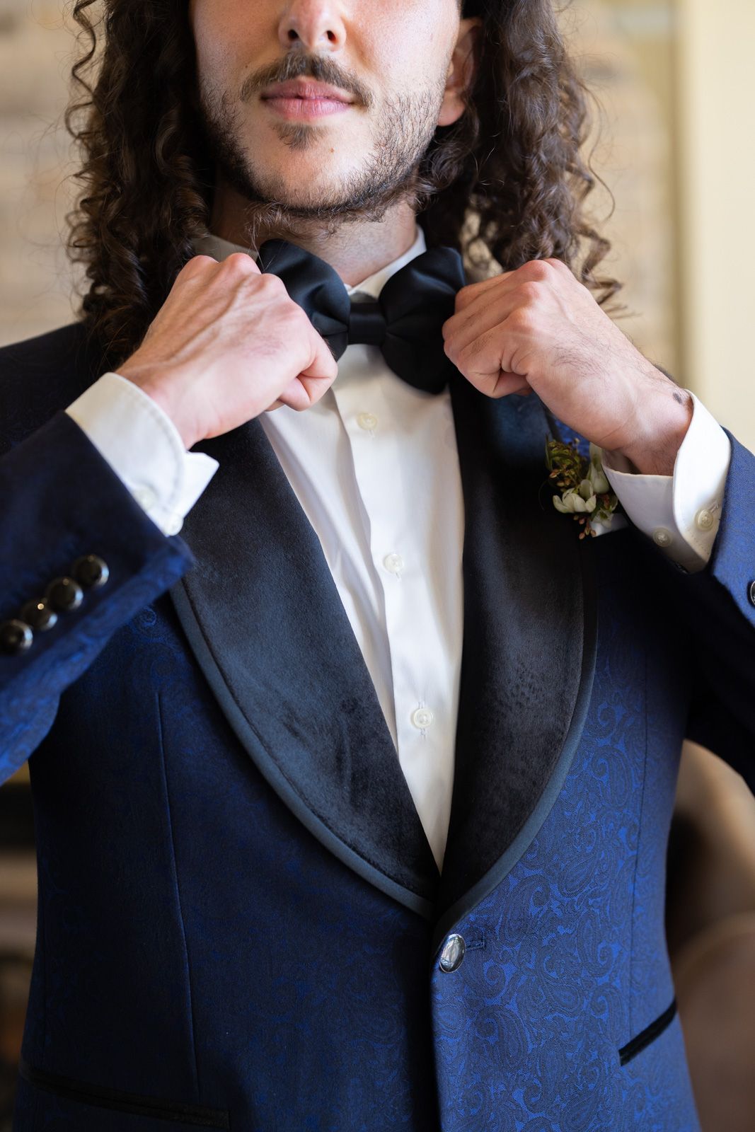 Close-up of person adjusting black bow tie while wearing navy tuxedo with satin lapels.