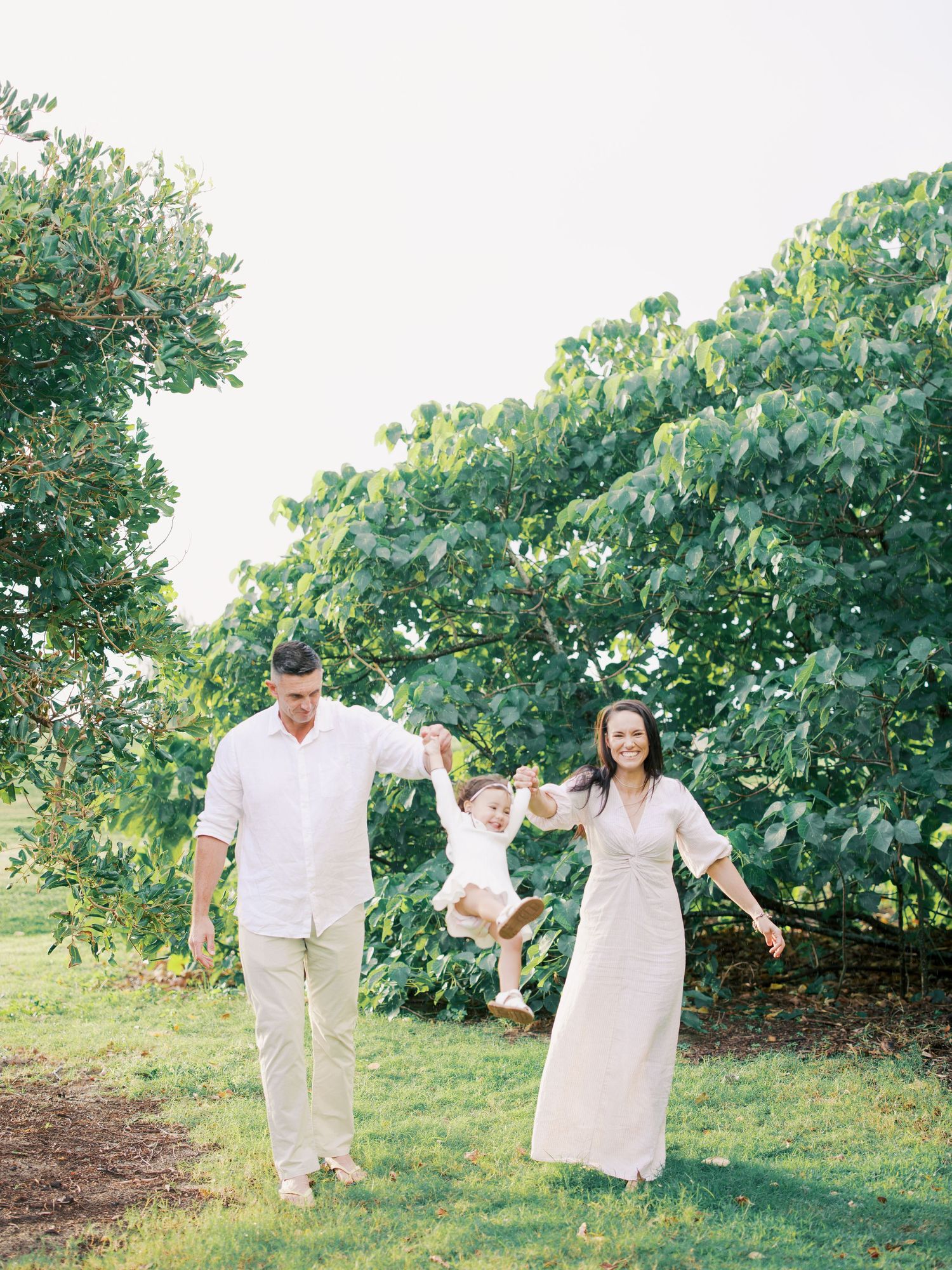 Family in white outfits walking through a lush garden setting during a photo session.