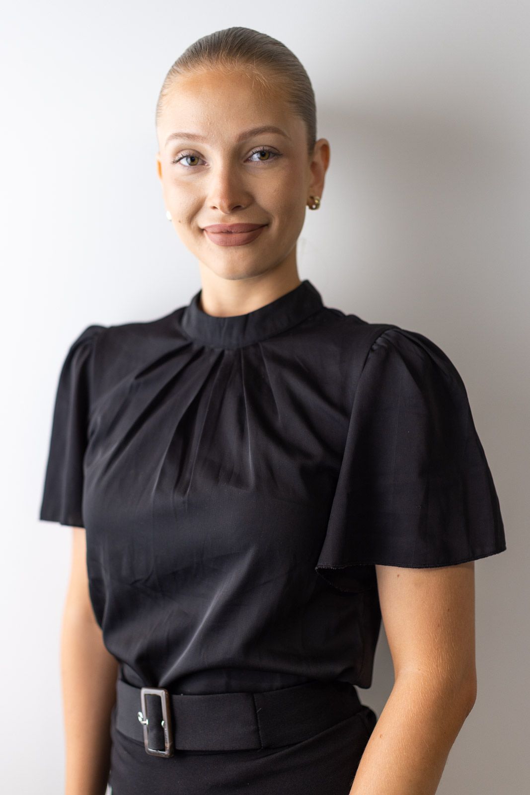 Person wearing a black short-sleeved dress with gathered neckline detail shown in three similar poses.