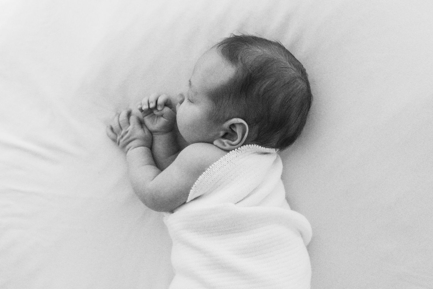 Black and white photo of sleeping newborn baby in white onesie.