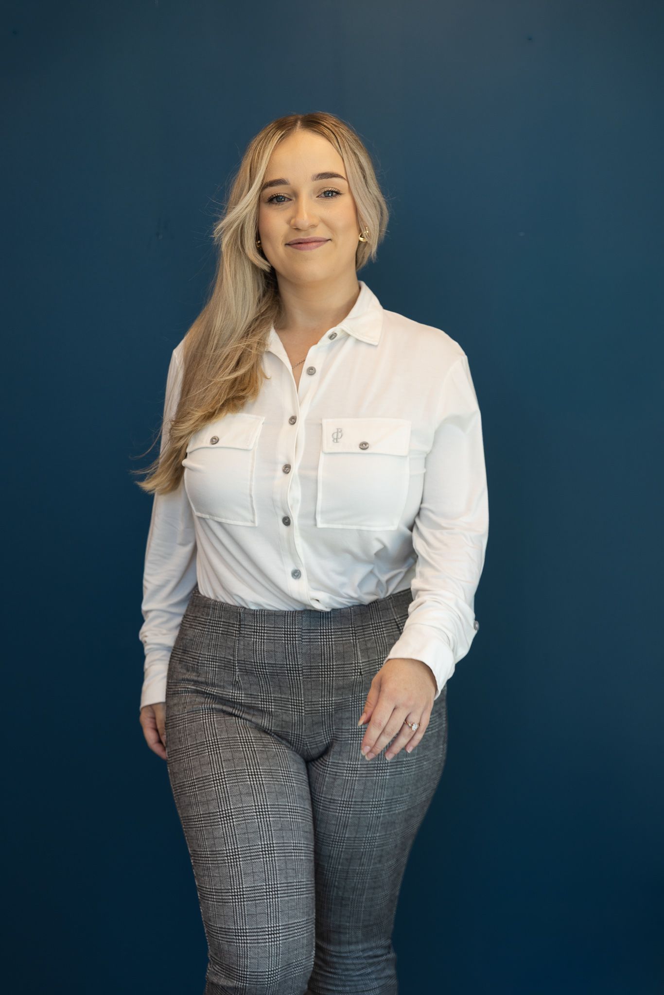 White button-up shirt styled with grey plaid pants against dark blue background.