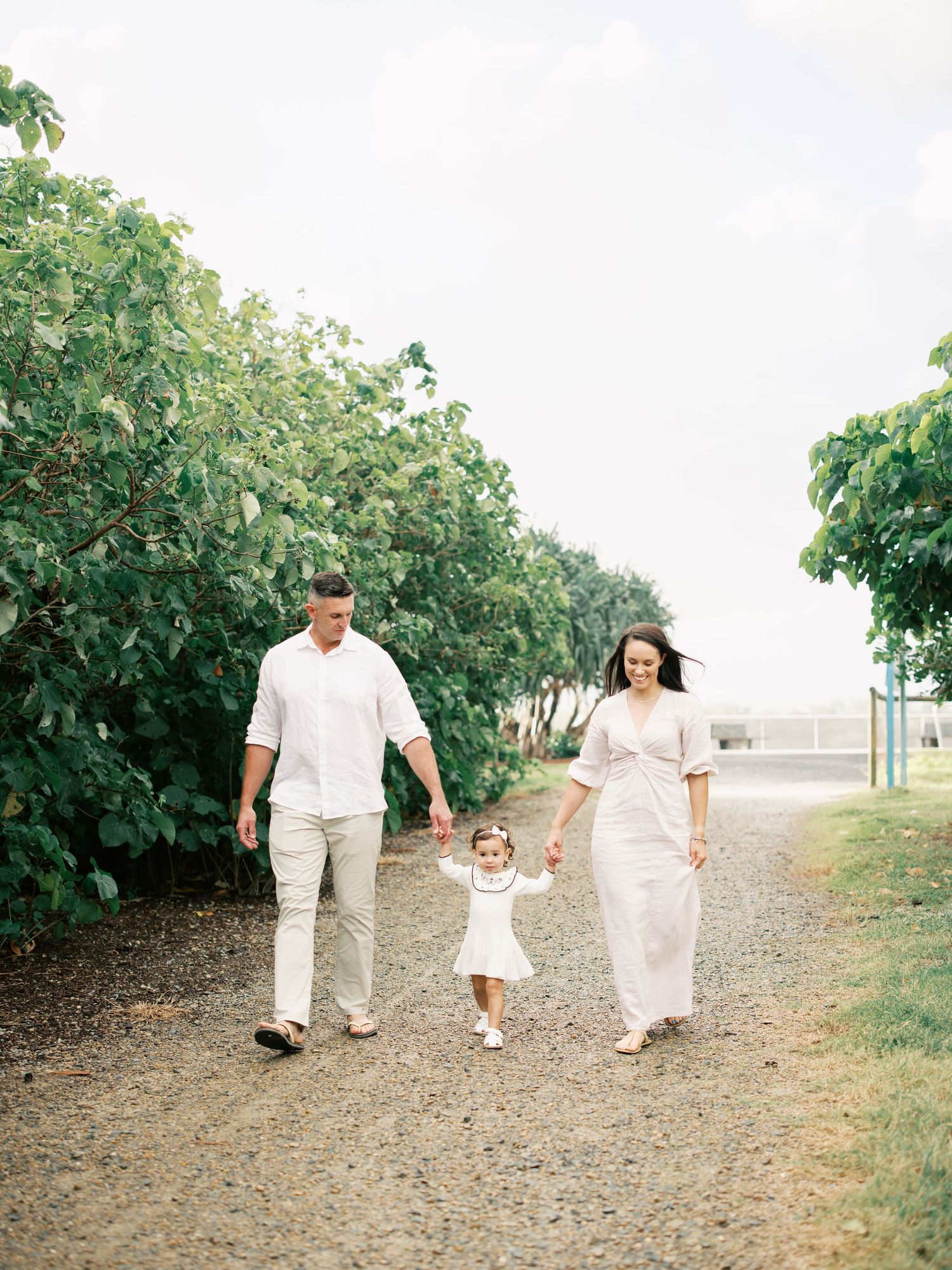 Family walking together on a garden path wearing coordinated white outfits.