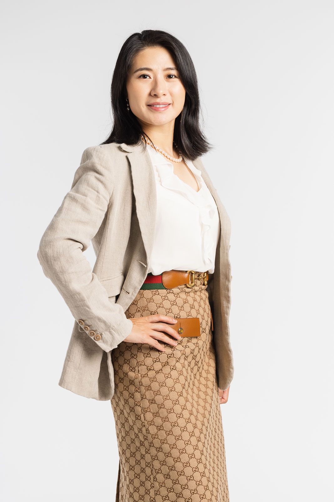 Woman wearing beige blazer, white blouse and brown patterned skirt poses in professional business attire.