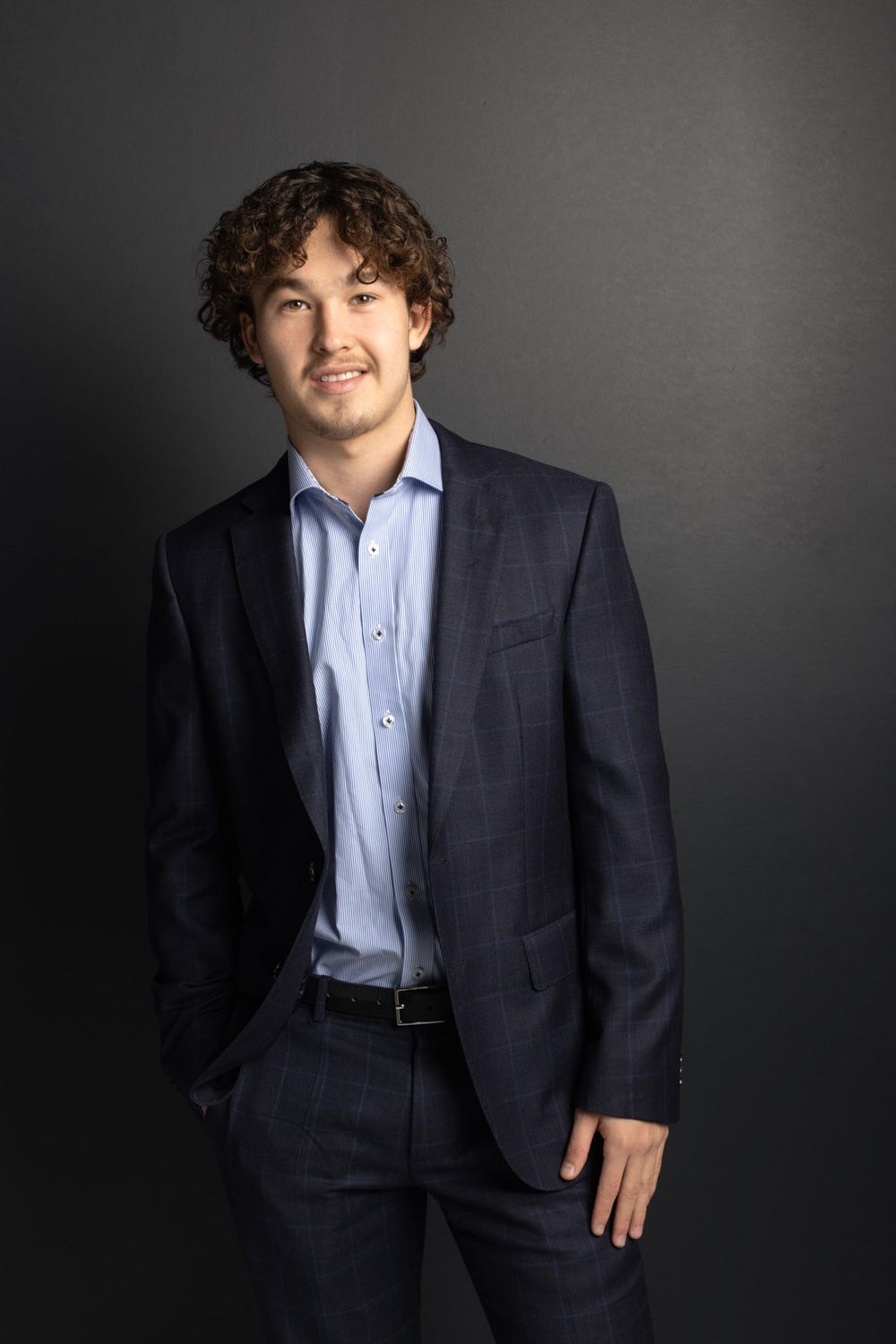 Professional headshots of man in navy suit and light blue shirt against dark background.