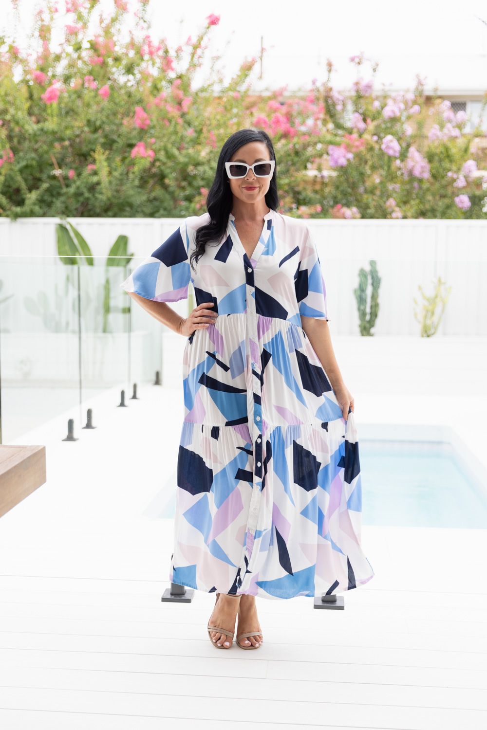 Geometric print maxi dress in blue and pink tones photographed by poolside with flowers.