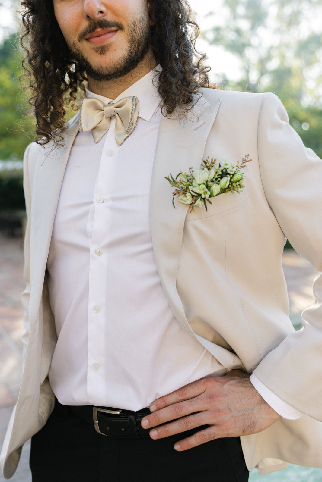 Close-up of a cream suit jacket with bow tie and floral boutonniere in an elegant wedding attire detail shot.