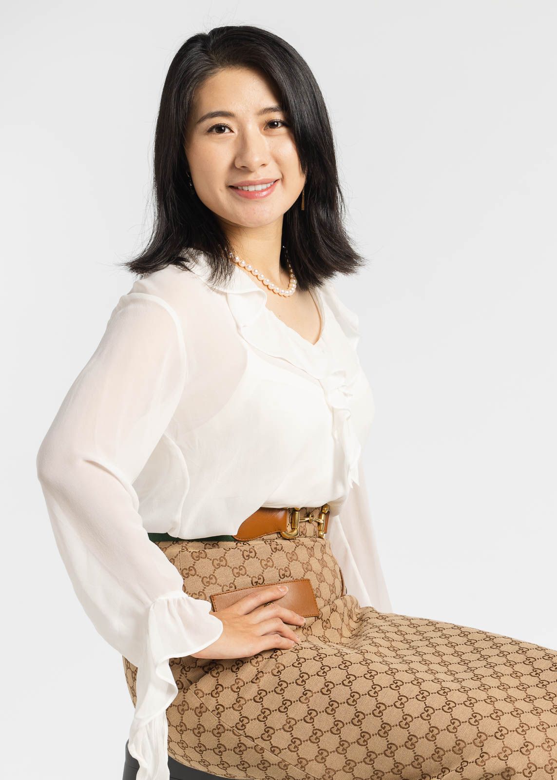A person in a white blouse poses with a brown monogram patterned fabric in a studio setting.