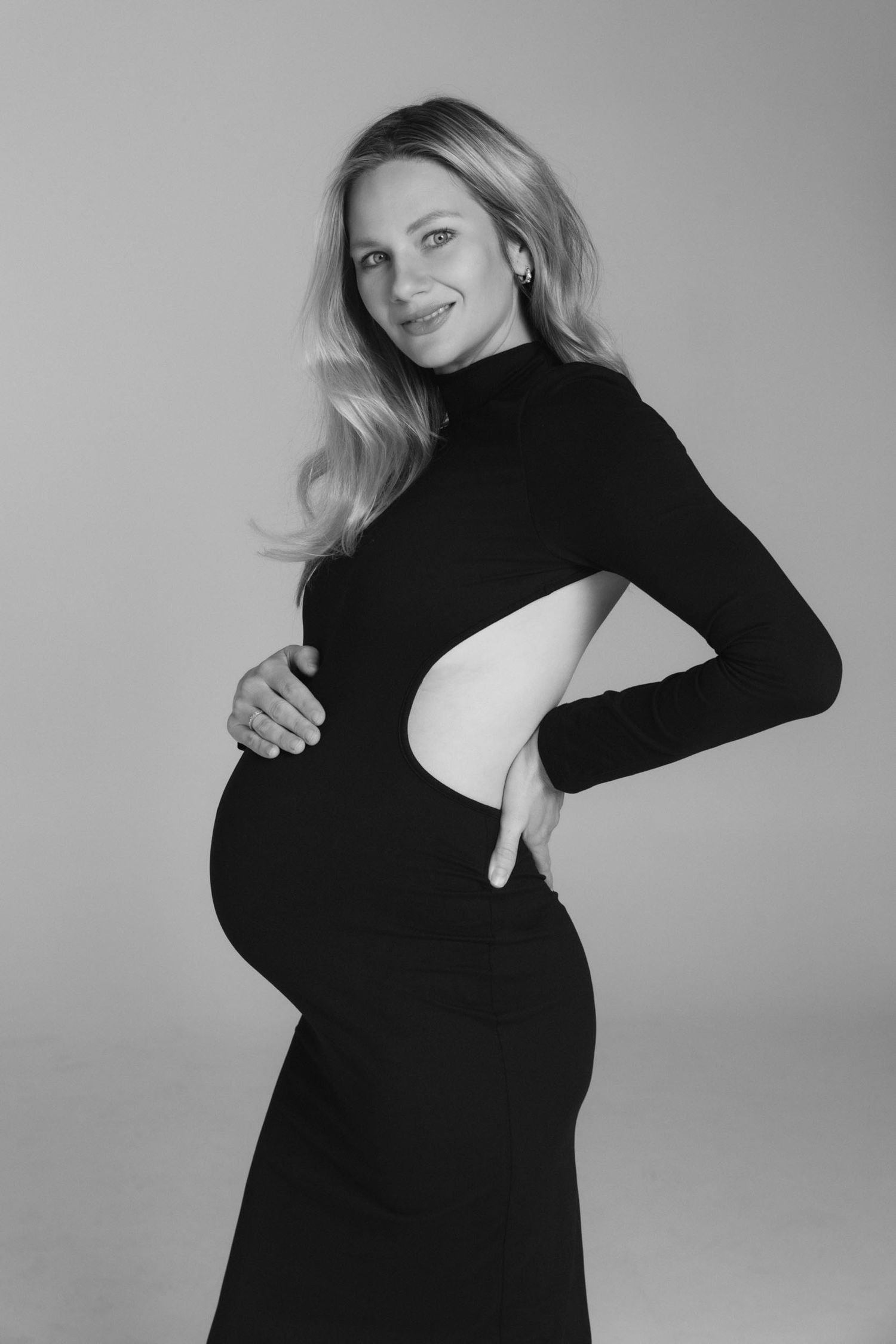 Elegant black and white maternity portrait featuring figure in fitted black turtleneck dress.