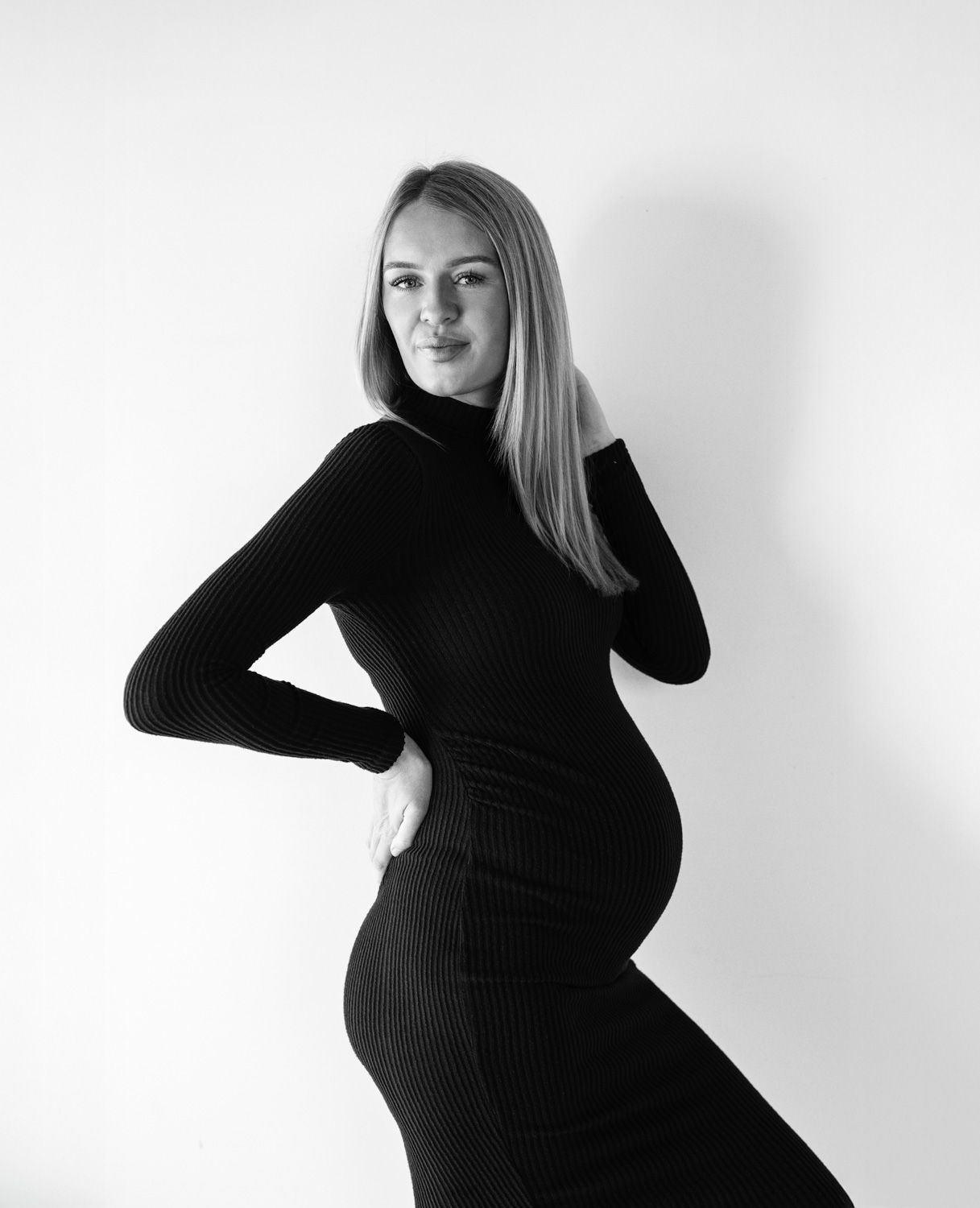 A black and white photo series shows a pregnant woman in a black dress posing against a white background.