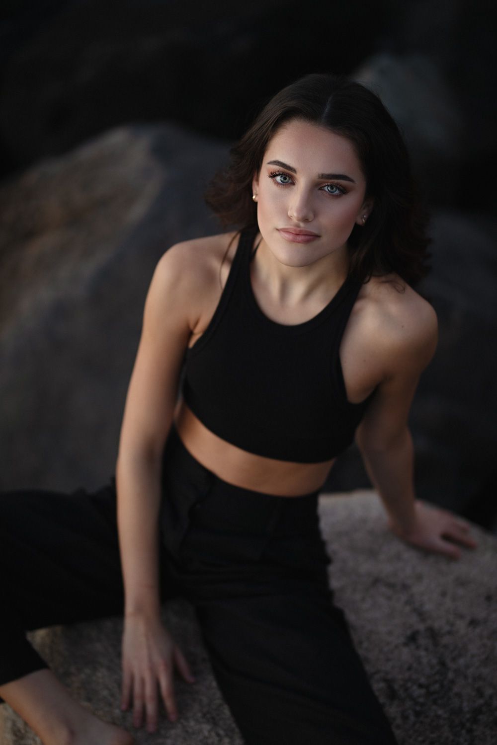 Athletic woman in black workout attire posed on rocky terrain at sunset.