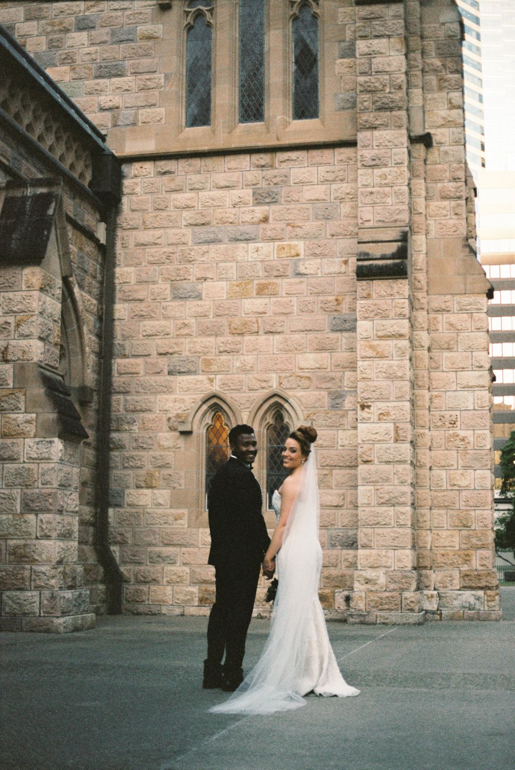 Bride and groom holding hands outside a historic stone church on their wedding day.