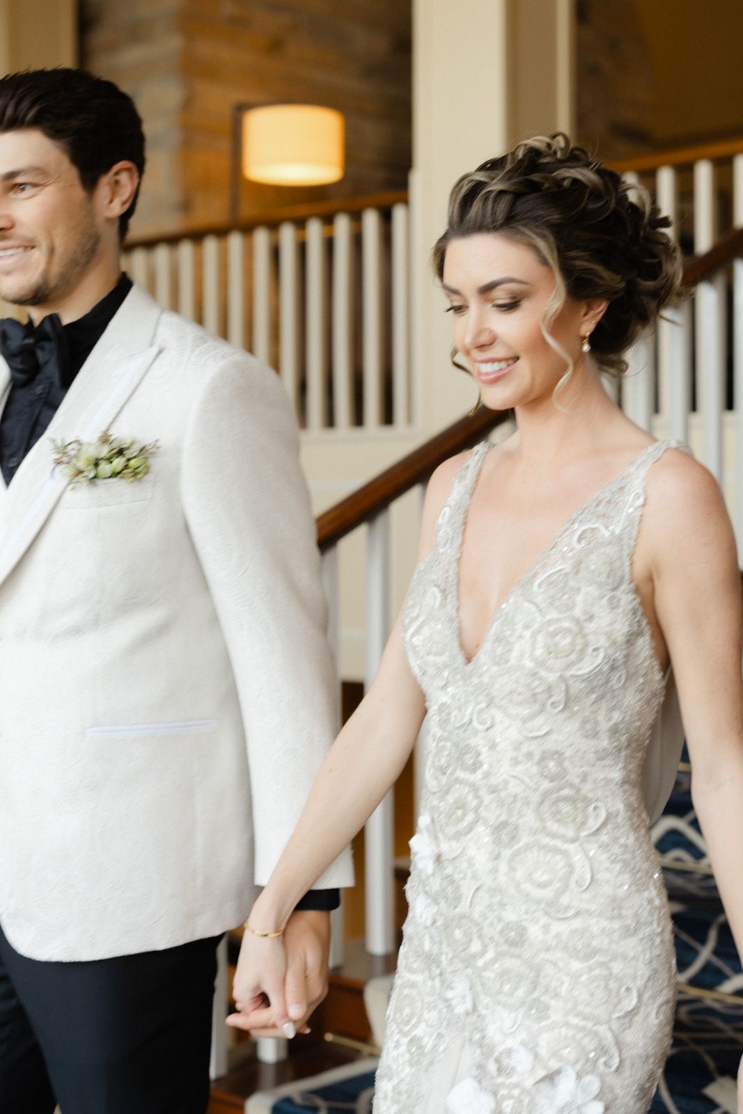 A wedding couple in coordinated white and black attire stand together on an elegant staircase.