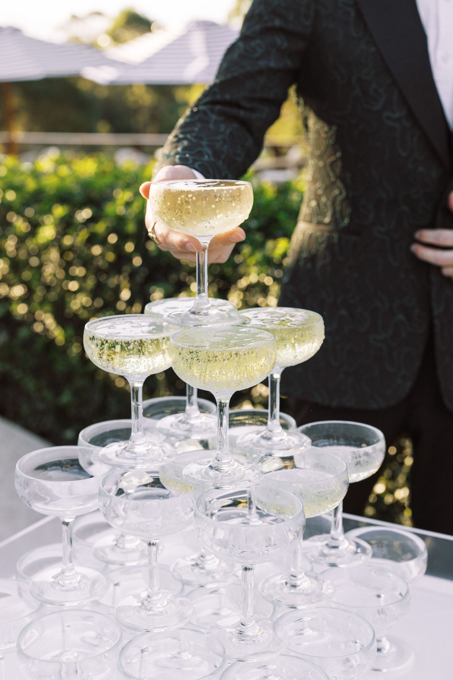 Elegant champagne tower setup with crystal coupe glasses at an outdoor wedding reception.