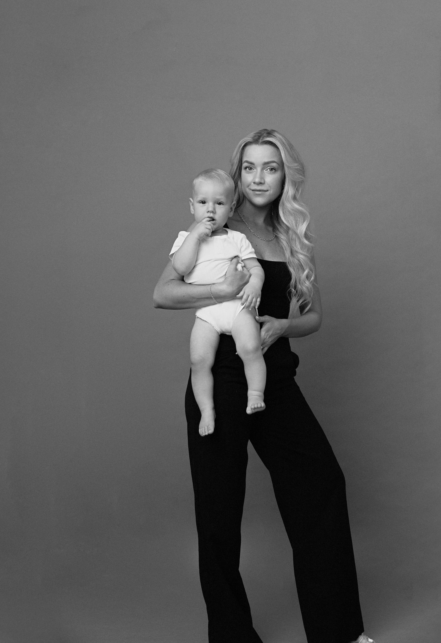 A black and white photo series showing a parent and baby in matching black outfits posing against a plain backdrop.
