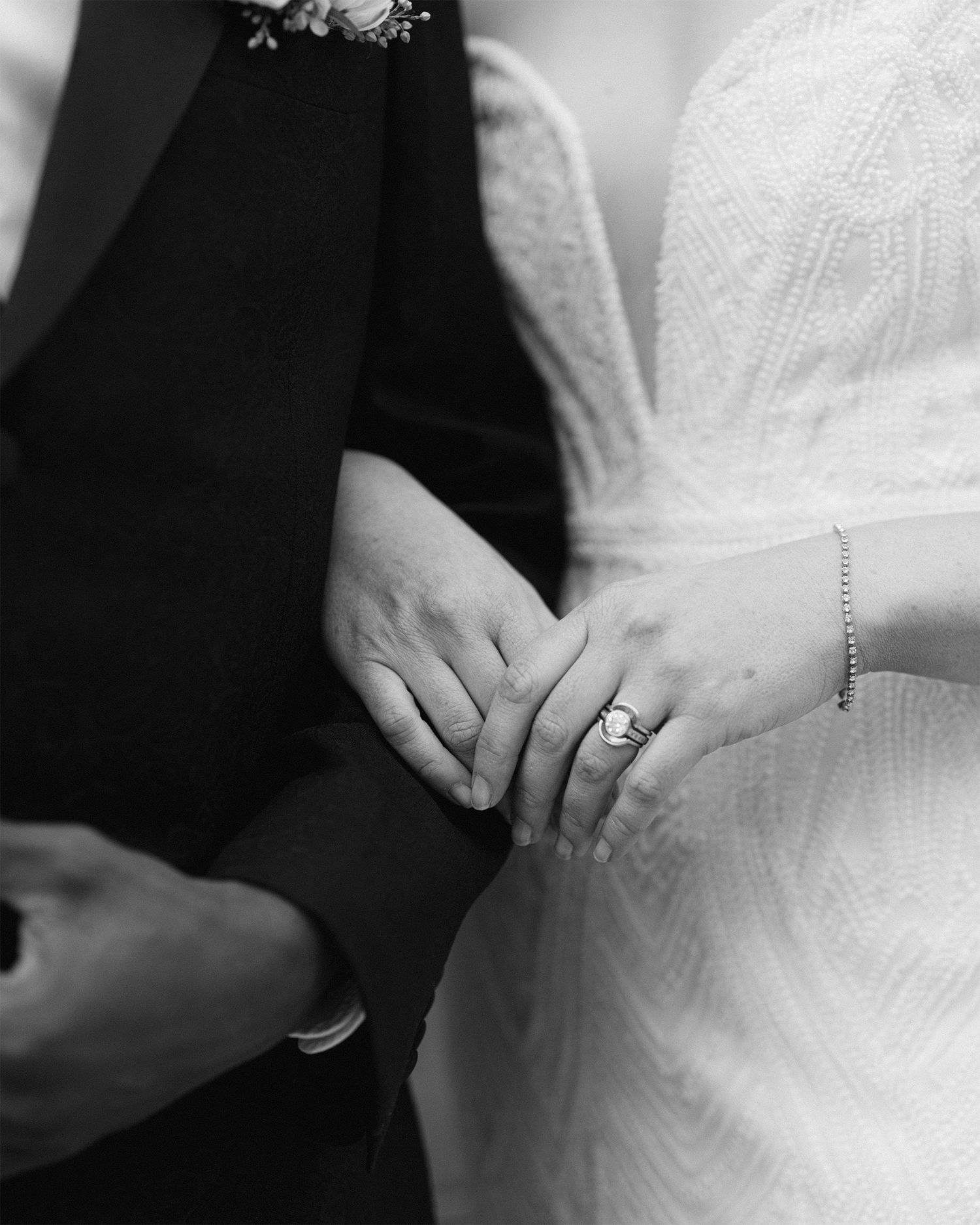 A close-up black and white photo of newlyweds' hands showing wedding rings.