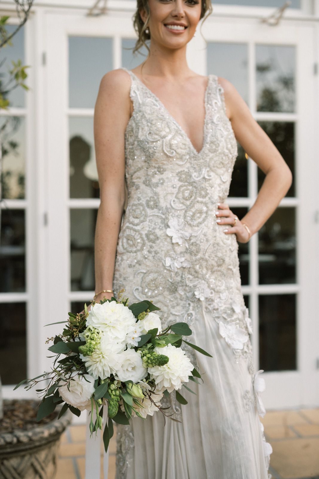 A close-up view of an elegant beaded wedding gown with floral details and a white bouquet featuring hydrangeas and greenery.