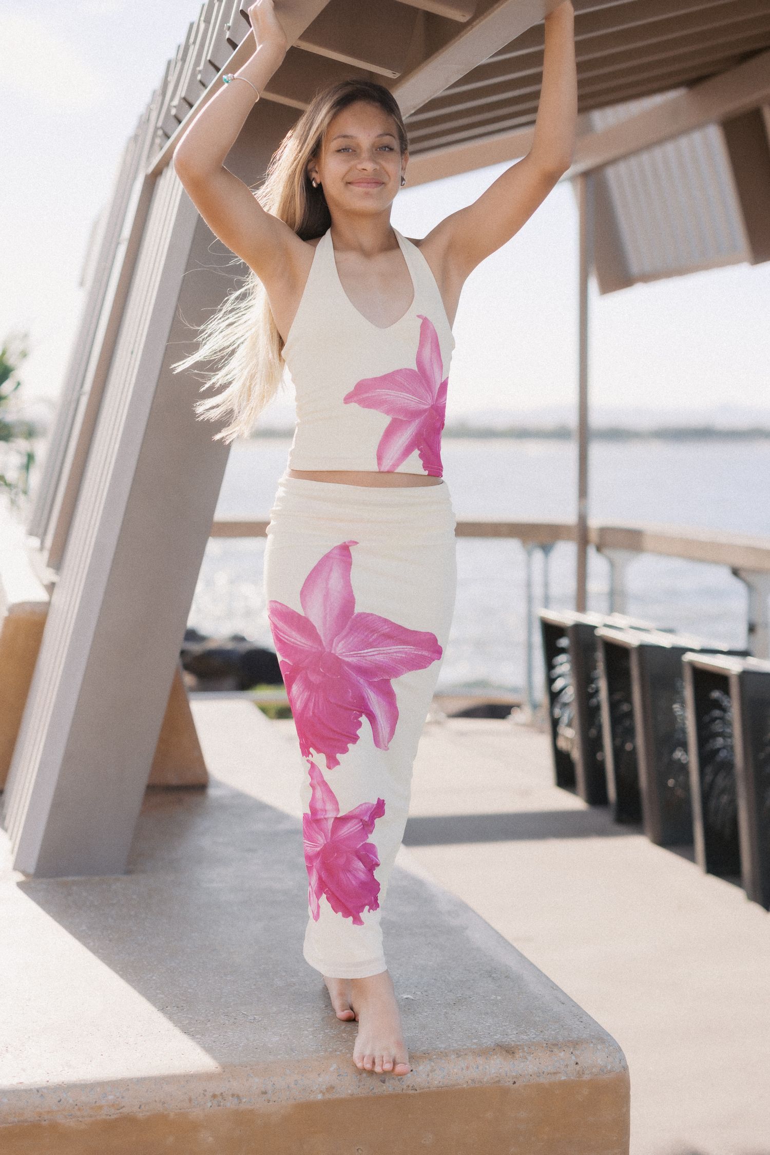 Woman wearing cream and pink floral halter crop top and matching maxi skirt set, posing outdoors near waterfront.