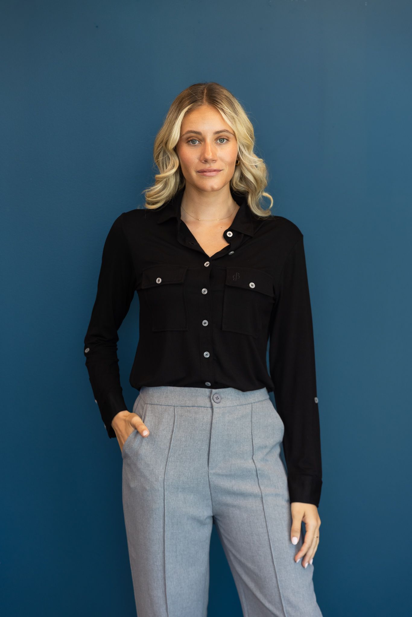 Professional fashion photos of black button-up shirt paired with grey trousers against blue backdrop.