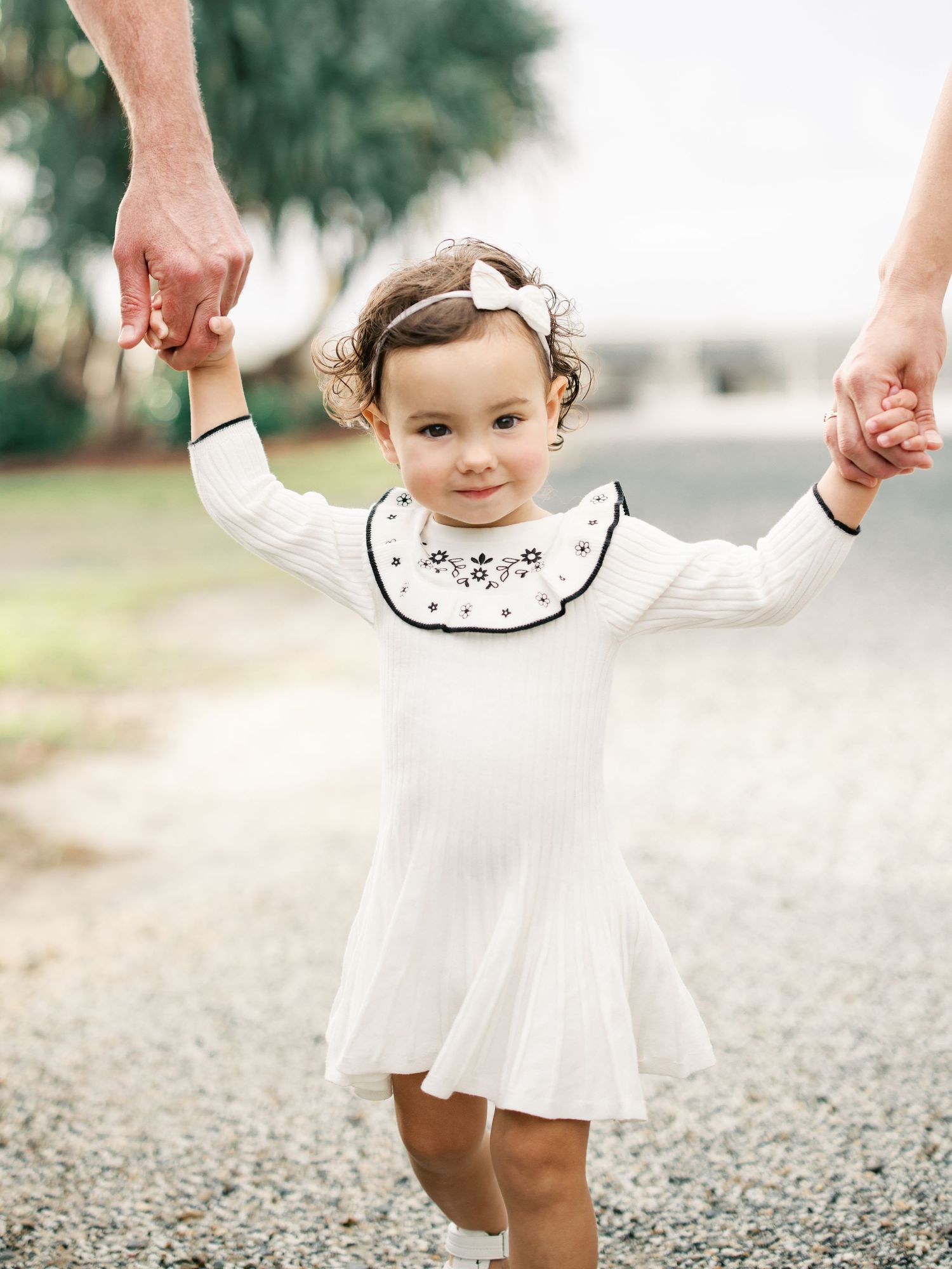 Young child in white dress twirling and playing during an outdoor photoshoot.