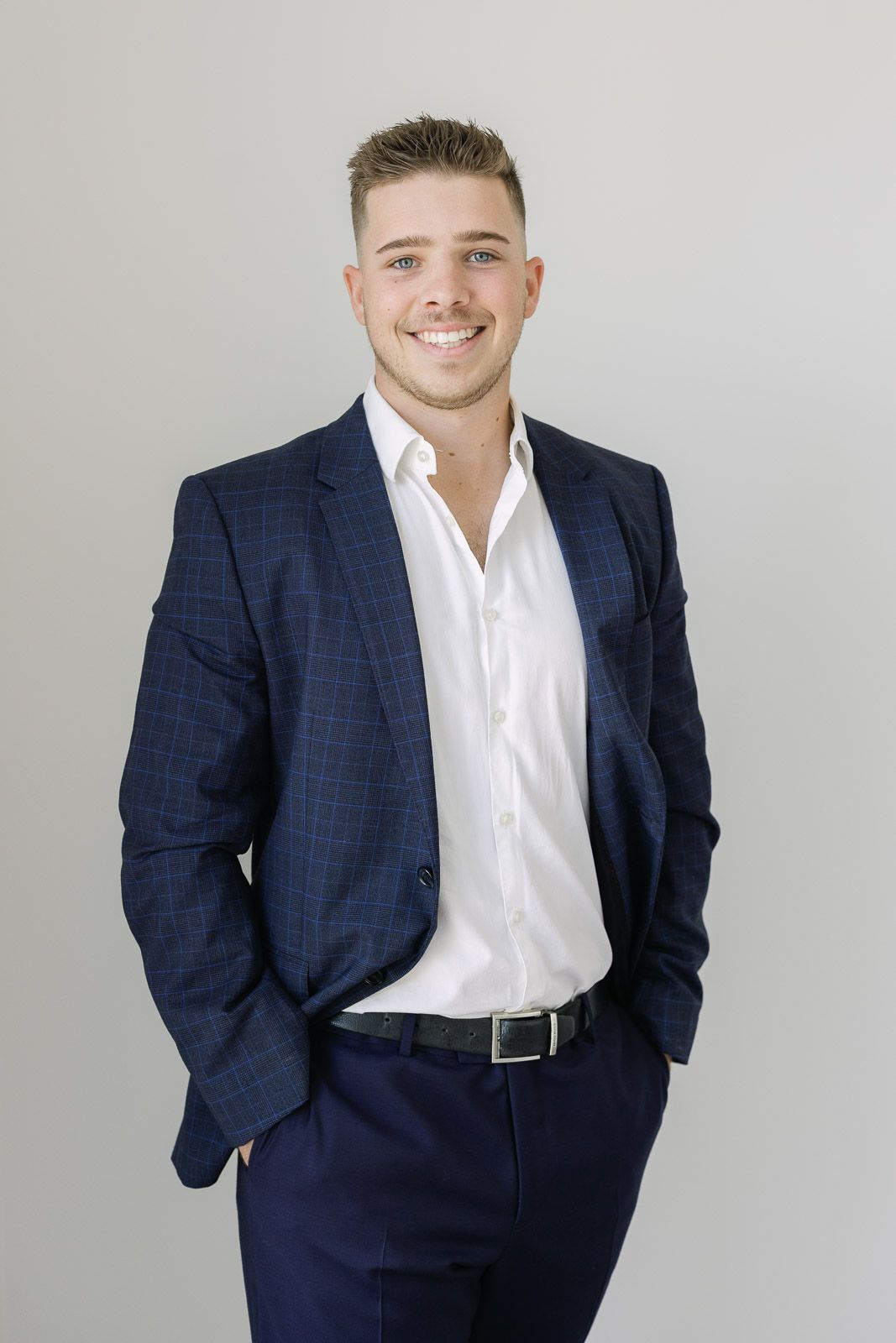 Professional headshot portrait of someone wearing a navy checkered suit jacket with white dress shirt.