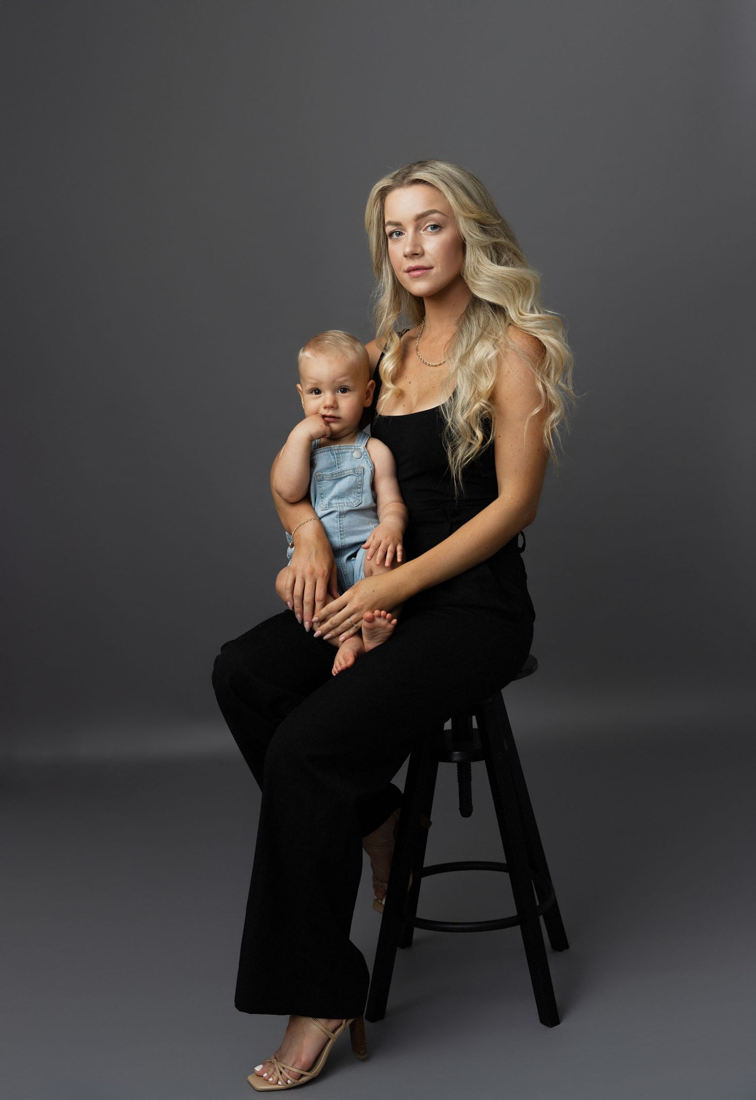 A series of four studio portraits showing a woman in black dress and toddler in denim against a gray backdrop.