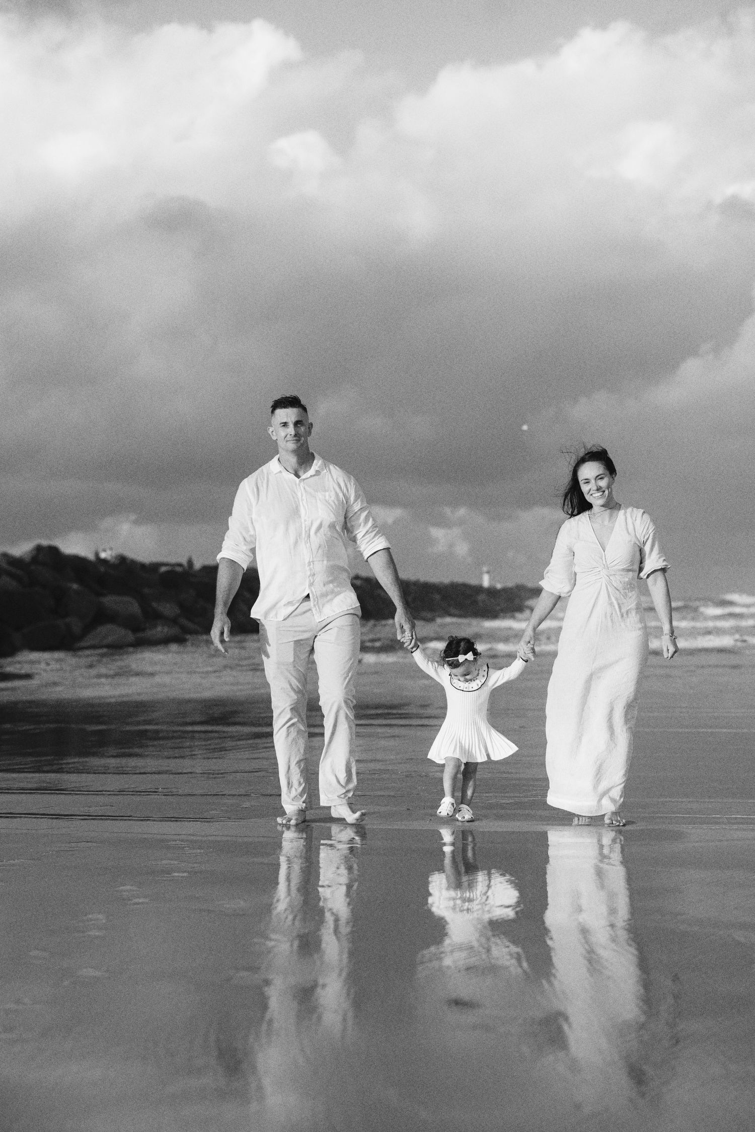 Black and white photo of family walking on reflective wet beach sand.