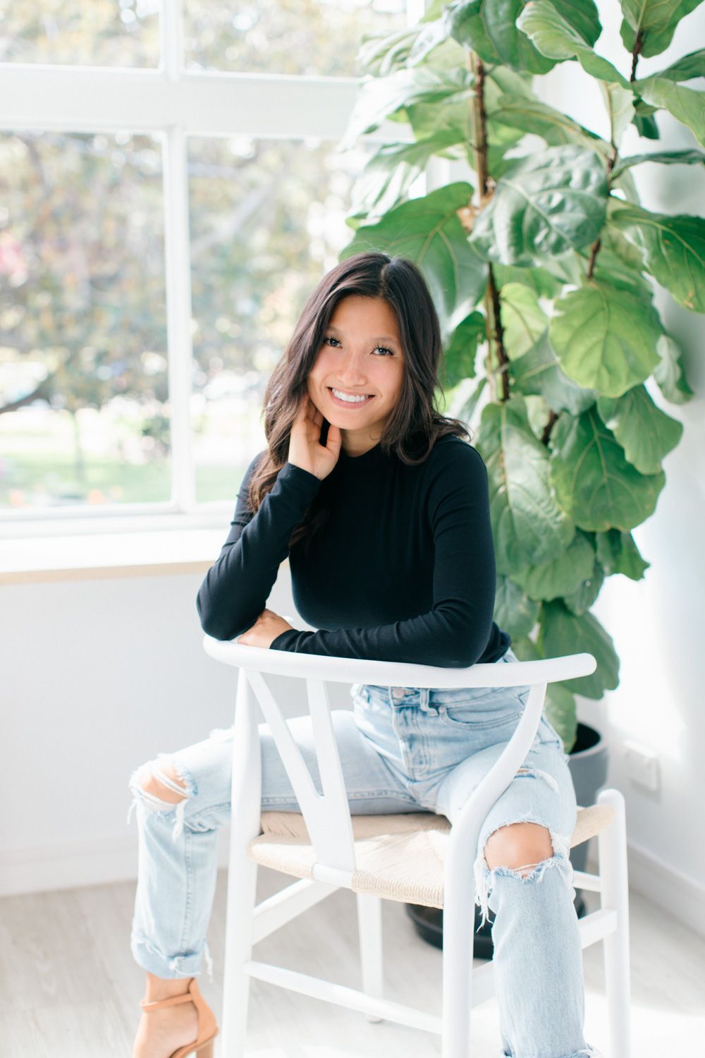 Lifestyle portraits near window with fiddle leaf fig plant featuring casual denim and black top outfit.