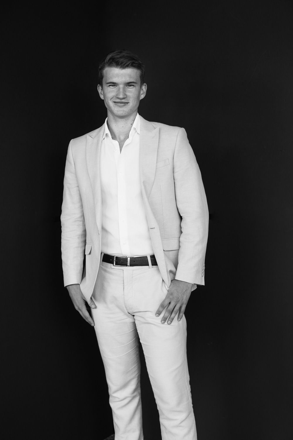Man in crisp white suit poses for professional portraits against black background.