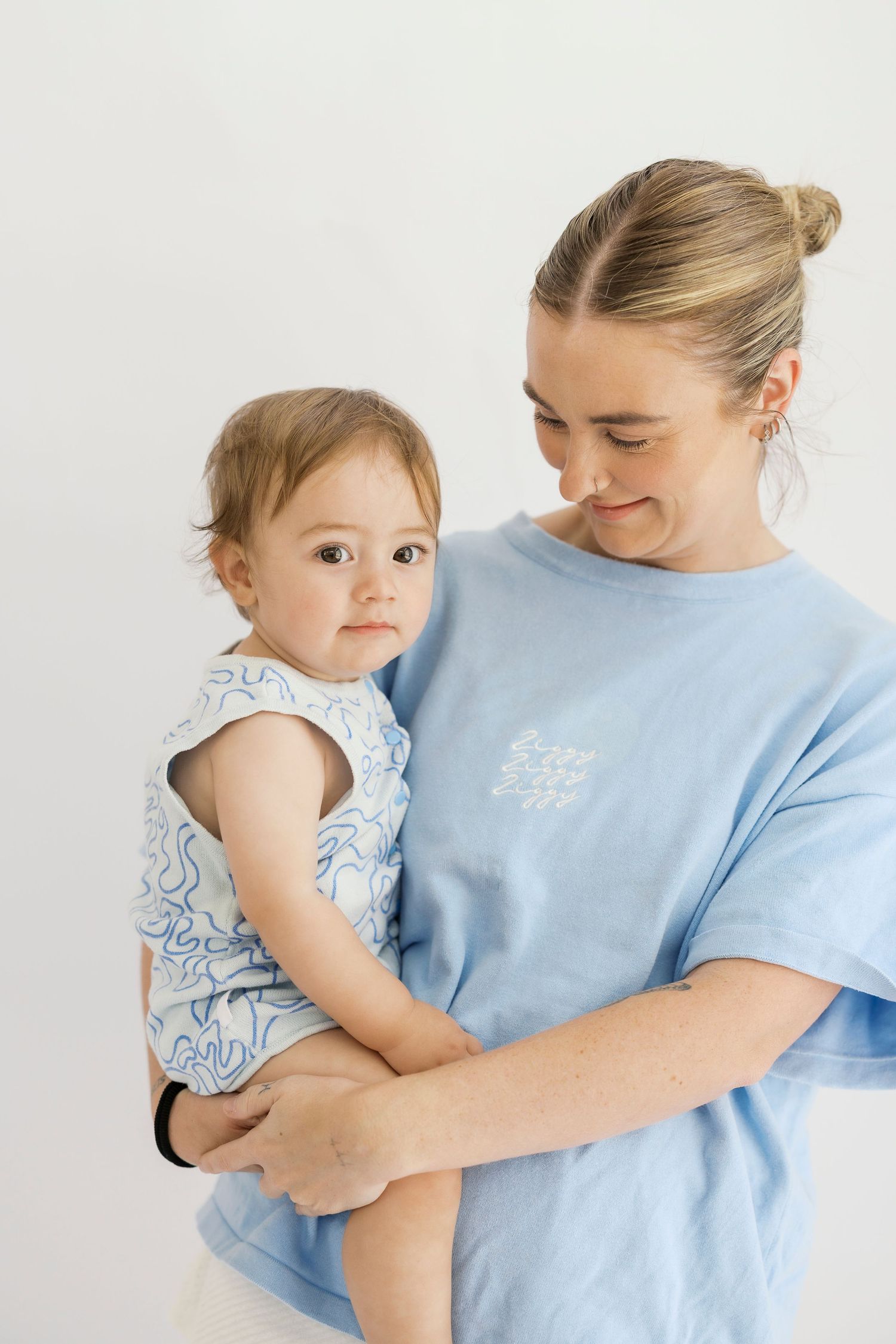 Parent and child wearing matching light blue outfits embrace in a tender moment against white background.