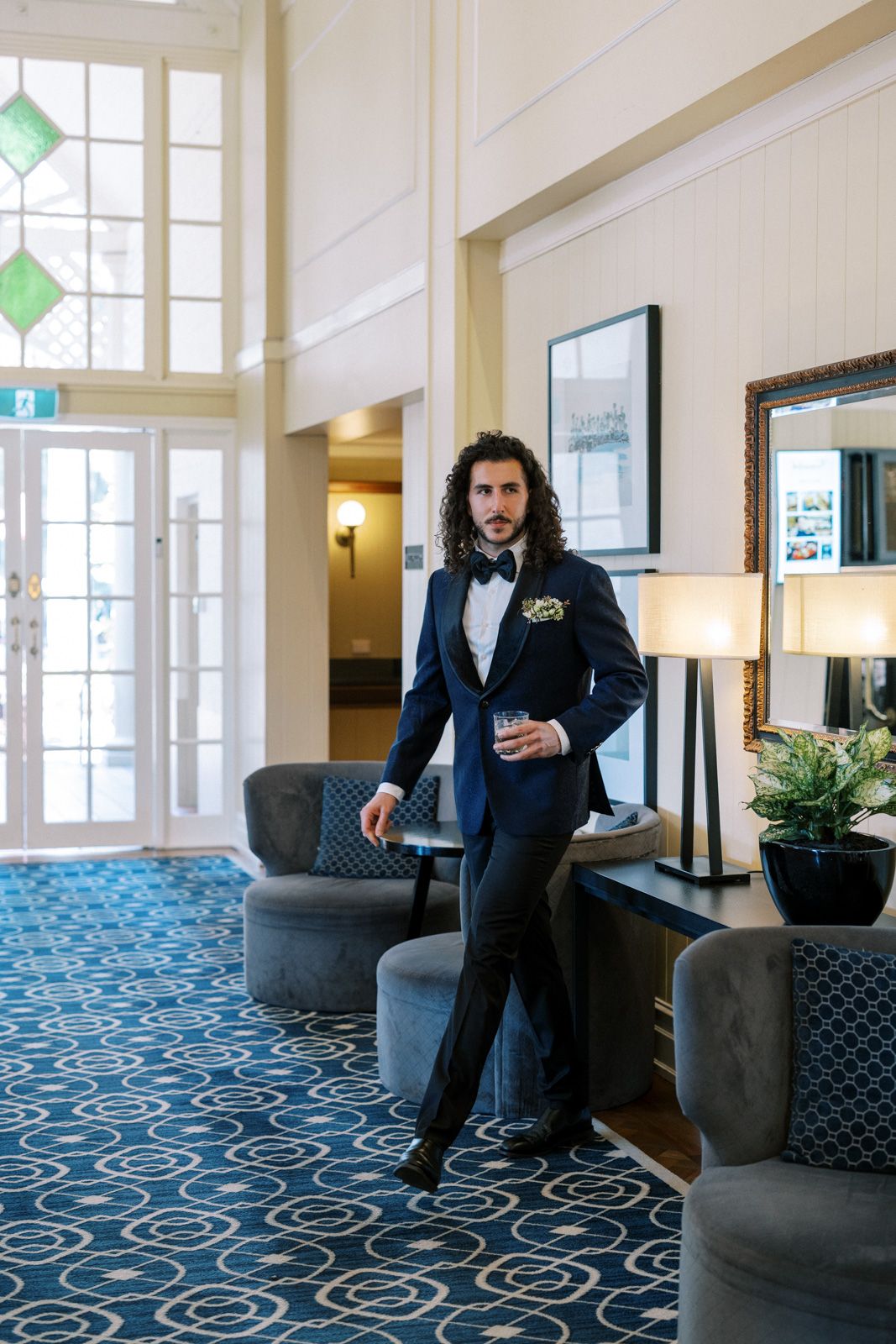 Elegant hotel lobby interior with blue patterned carpet, grey furniture and decorative green stained glass windows.