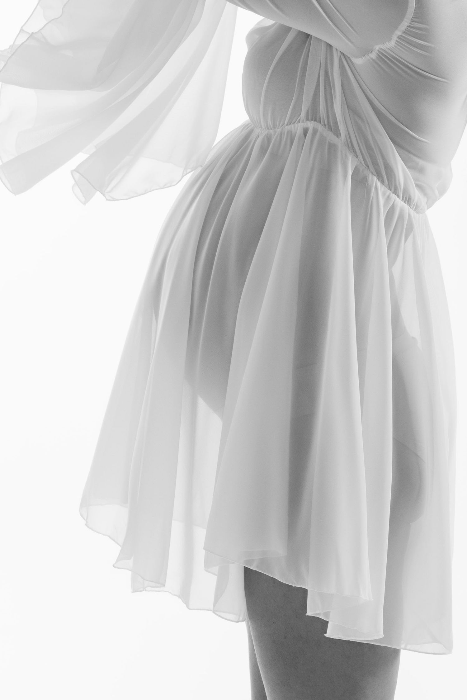 Artistic close-up of flowing white fabric dress against light background.