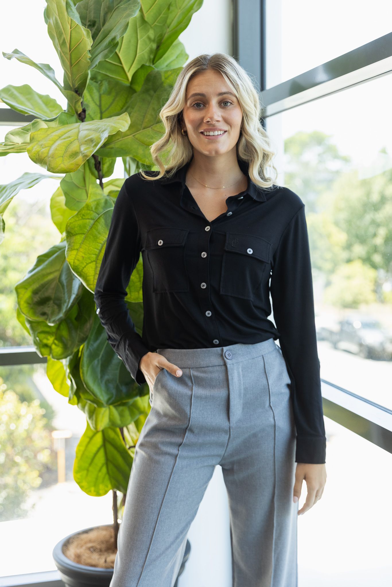 Casual business outfit featuring black shirt and grey pants photographed near indoor plant.