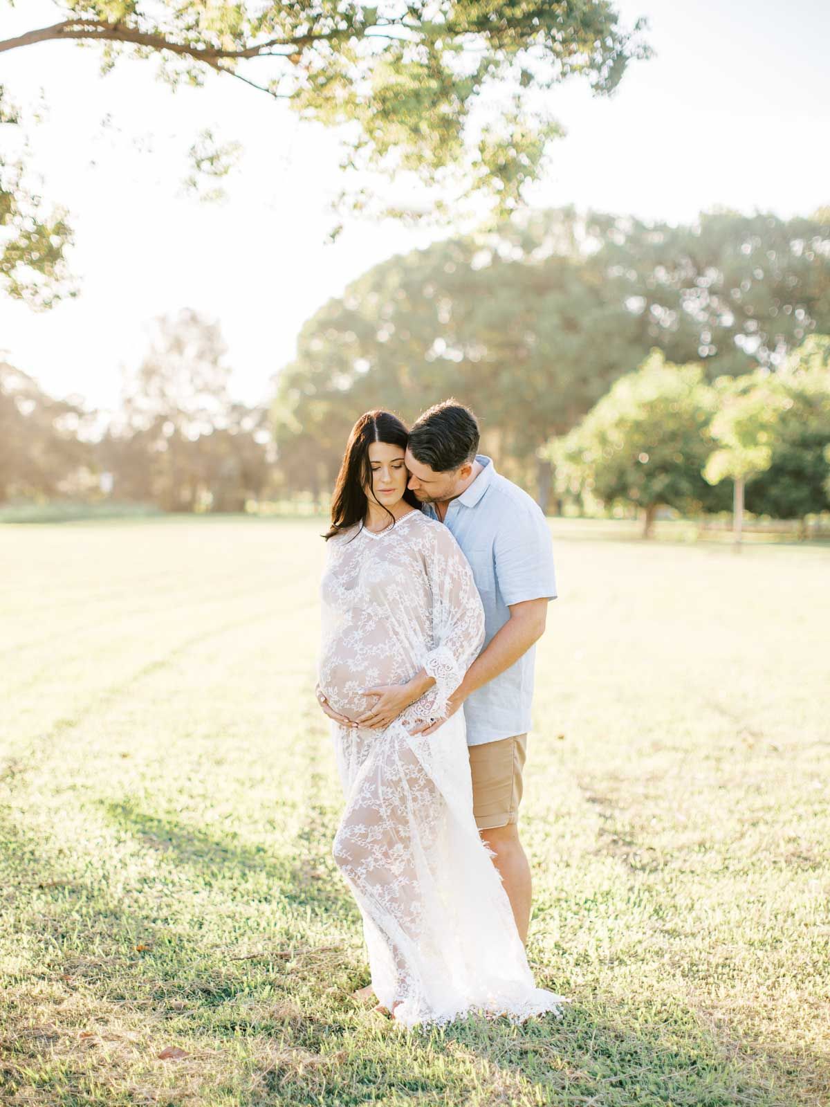 A tender maternity portrait in a sunlit field with a flowing lace dress.