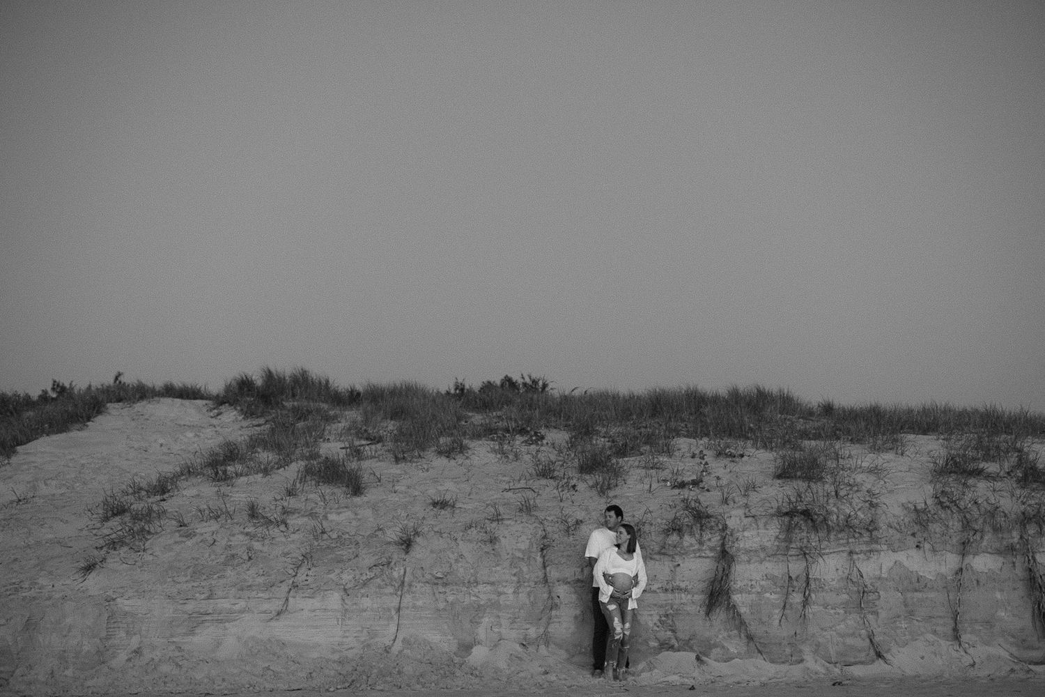 Black and white photograph of a desert landscape with barren trees and dry vegetation in the distance.