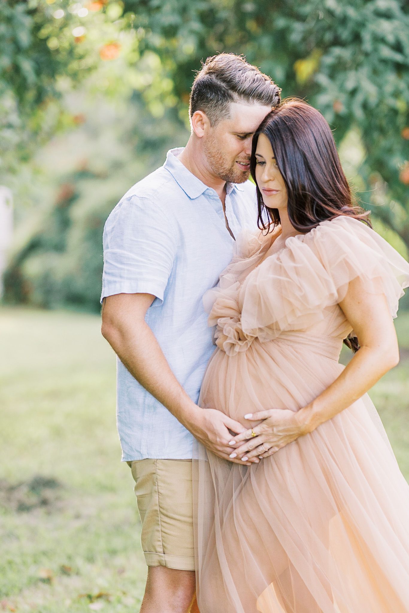 A romantic maternity photoshoot in a garden setting with soft peach dress and white shirt.