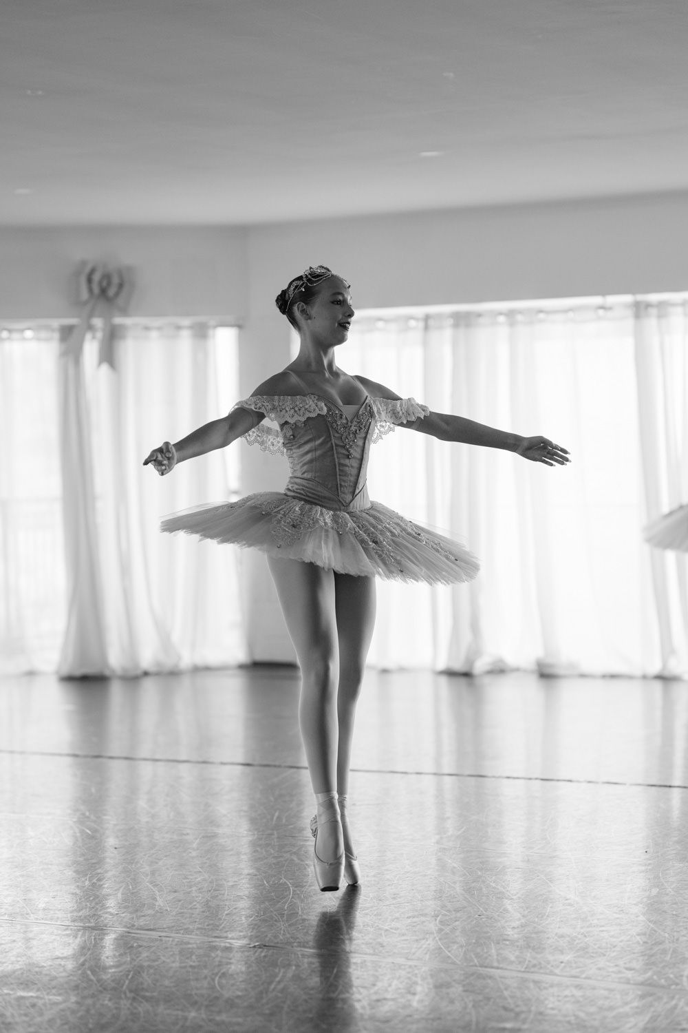 Black and white photo of a graceful ballerina in a tutu performing on pointe in a bright dance studio.