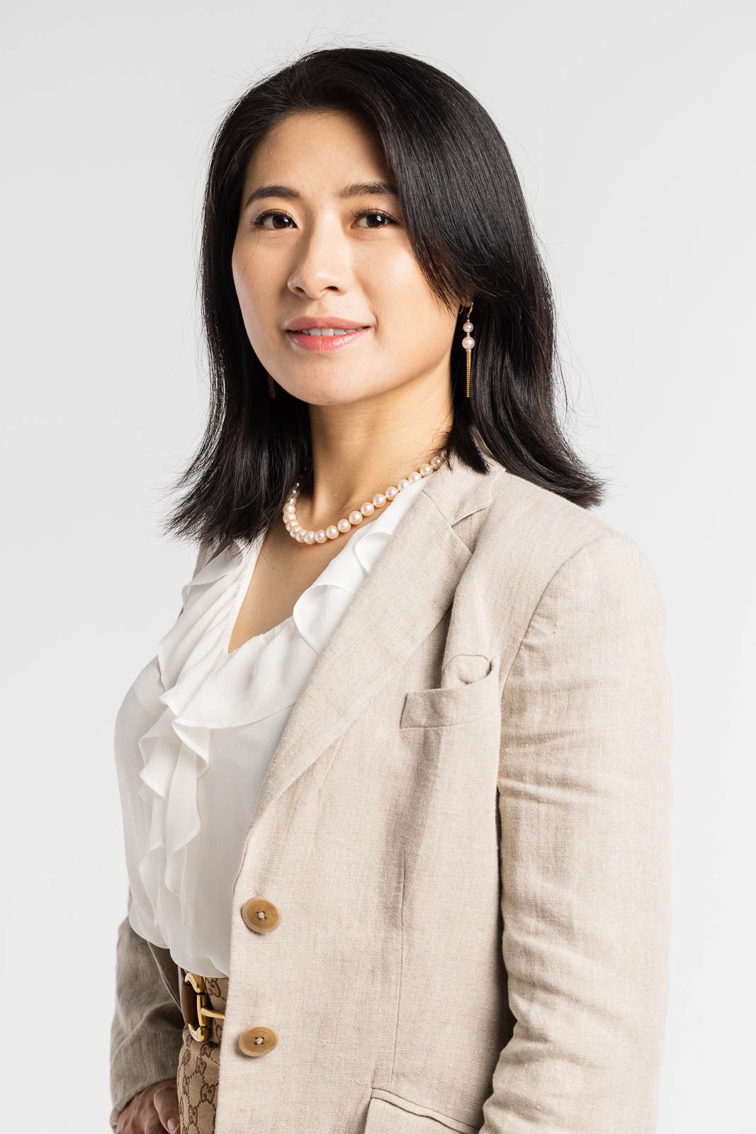 Professional headshot of someone wearing a beige blazer and white blouse against a light background.