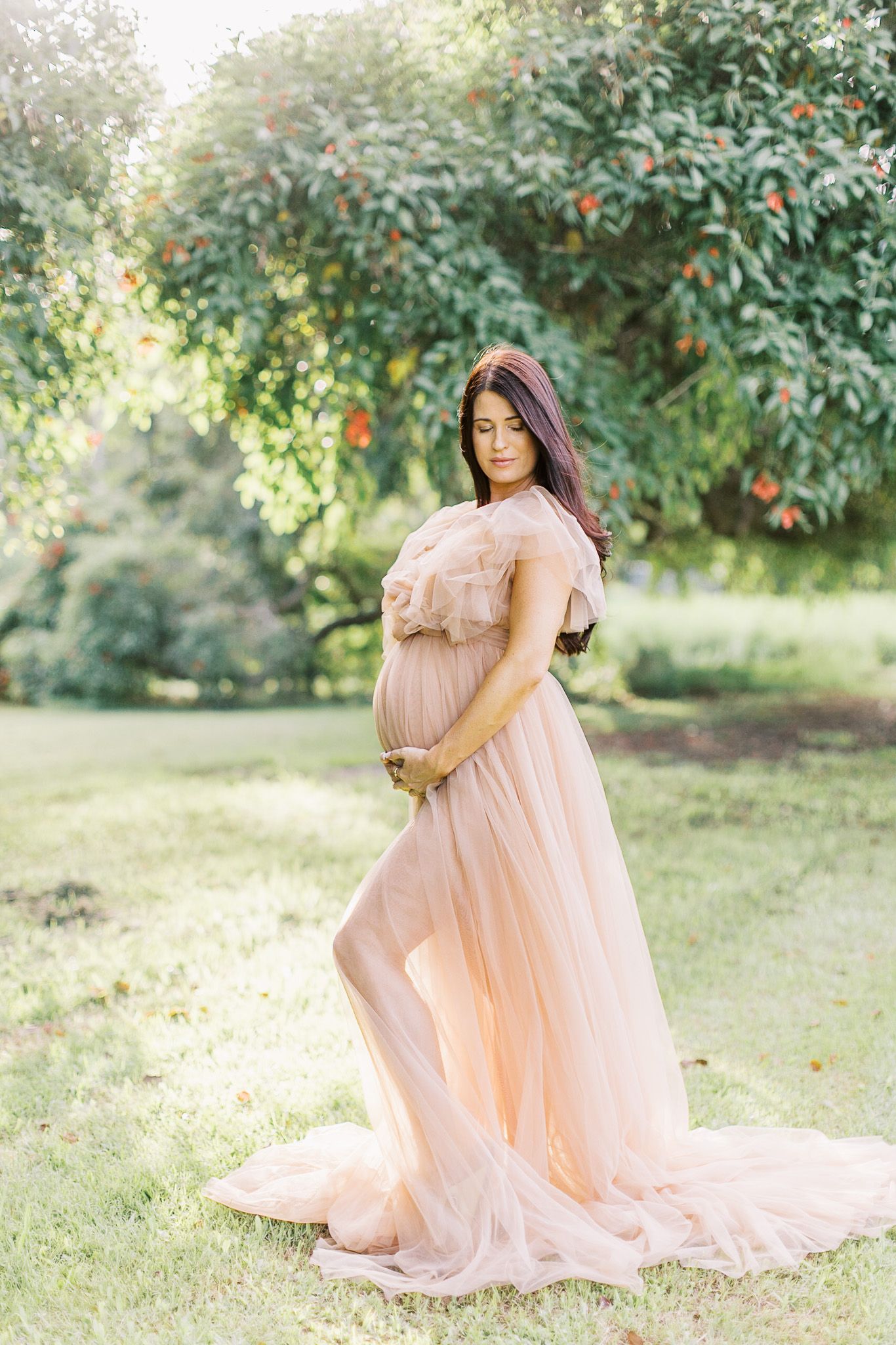 A person in a flowing peach-colored dress poses gracefully in a garden setting with lush greenery in the background.