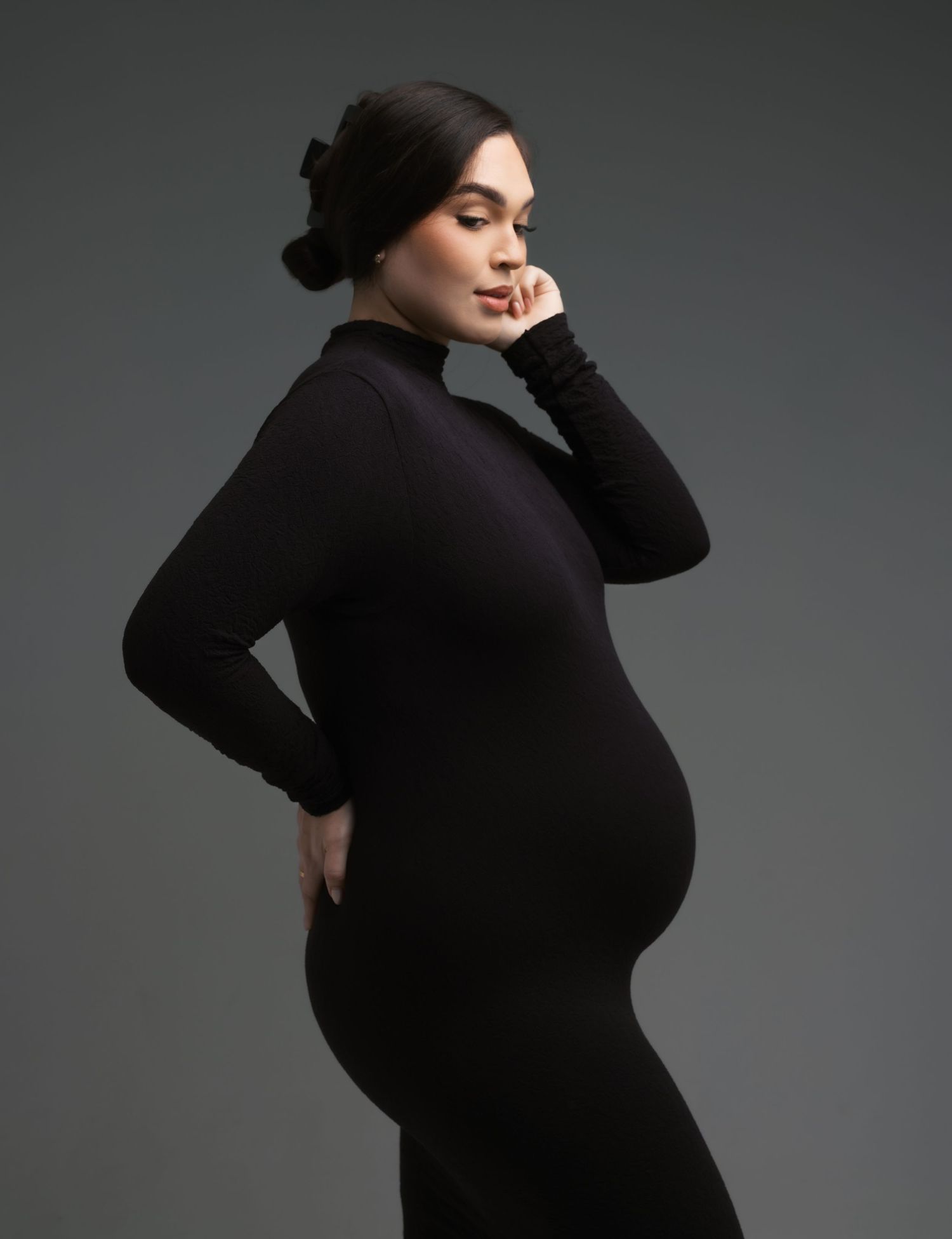 Dramatic maternity portraits in black dress against dark background with moody lighting.