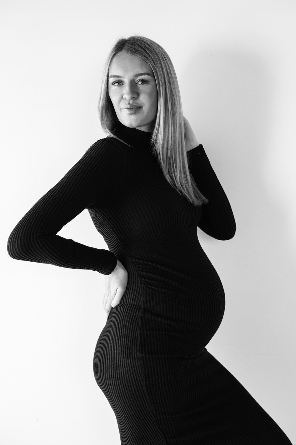 Black and white photo series showing silhouette of pregnant woman in turtleneck sweater posing against white background.