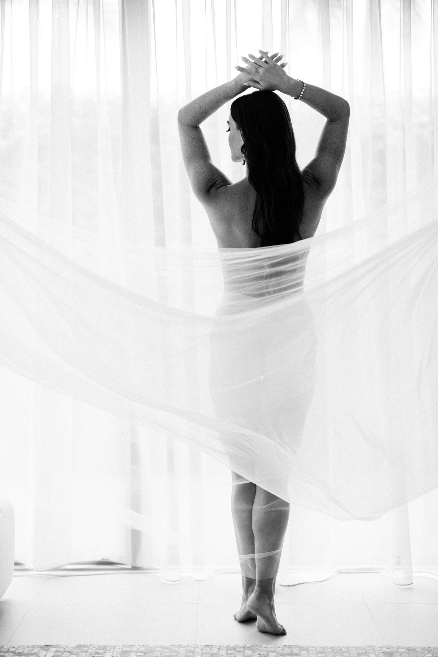 Back view of woman in white dress with flowing fabric in ethereal boudoir setting.