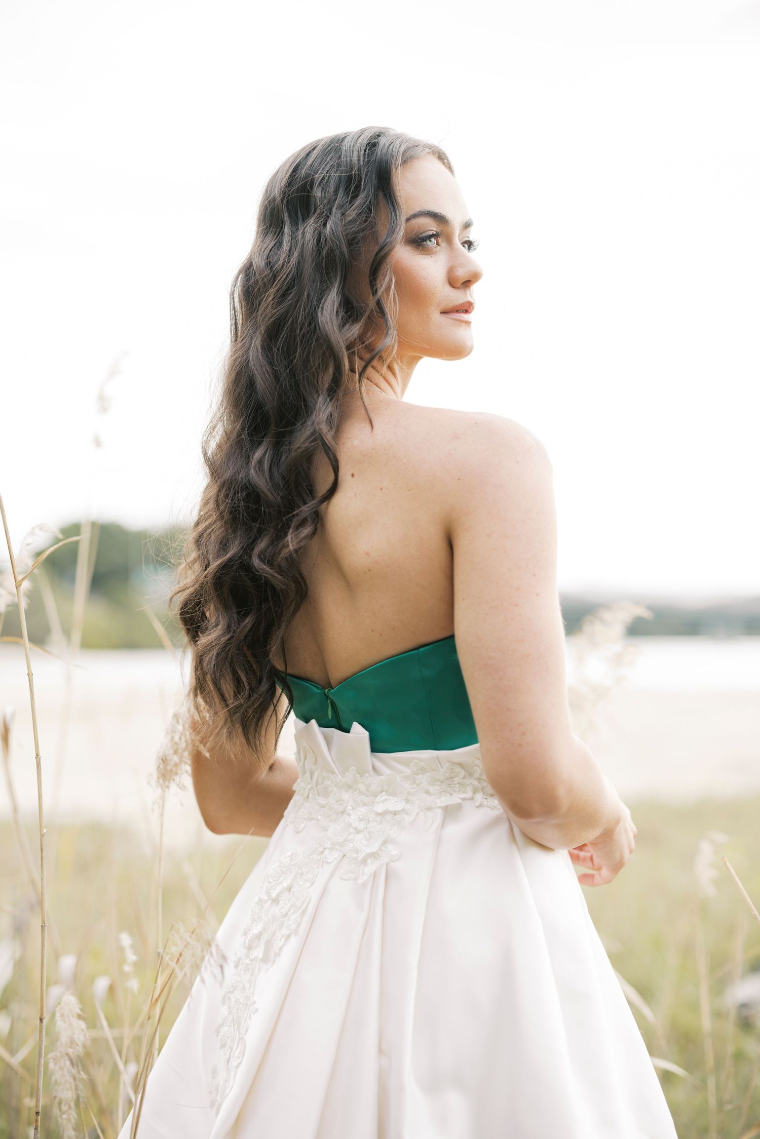 Elegant woman in white dress with green bodice poses in natural outdoor setting.